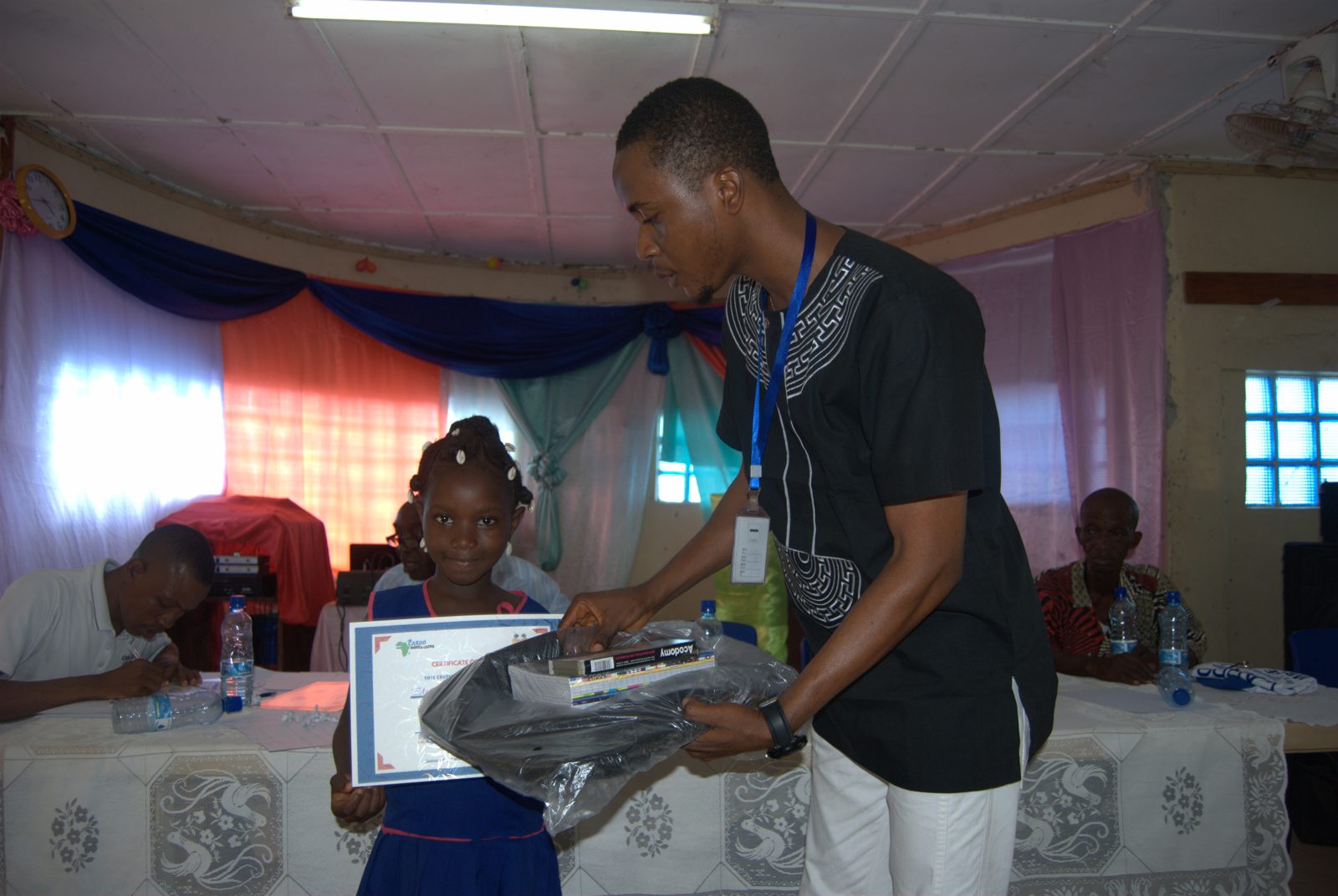 A CARDO staff member presenting a certificate and school supplies to a pupil