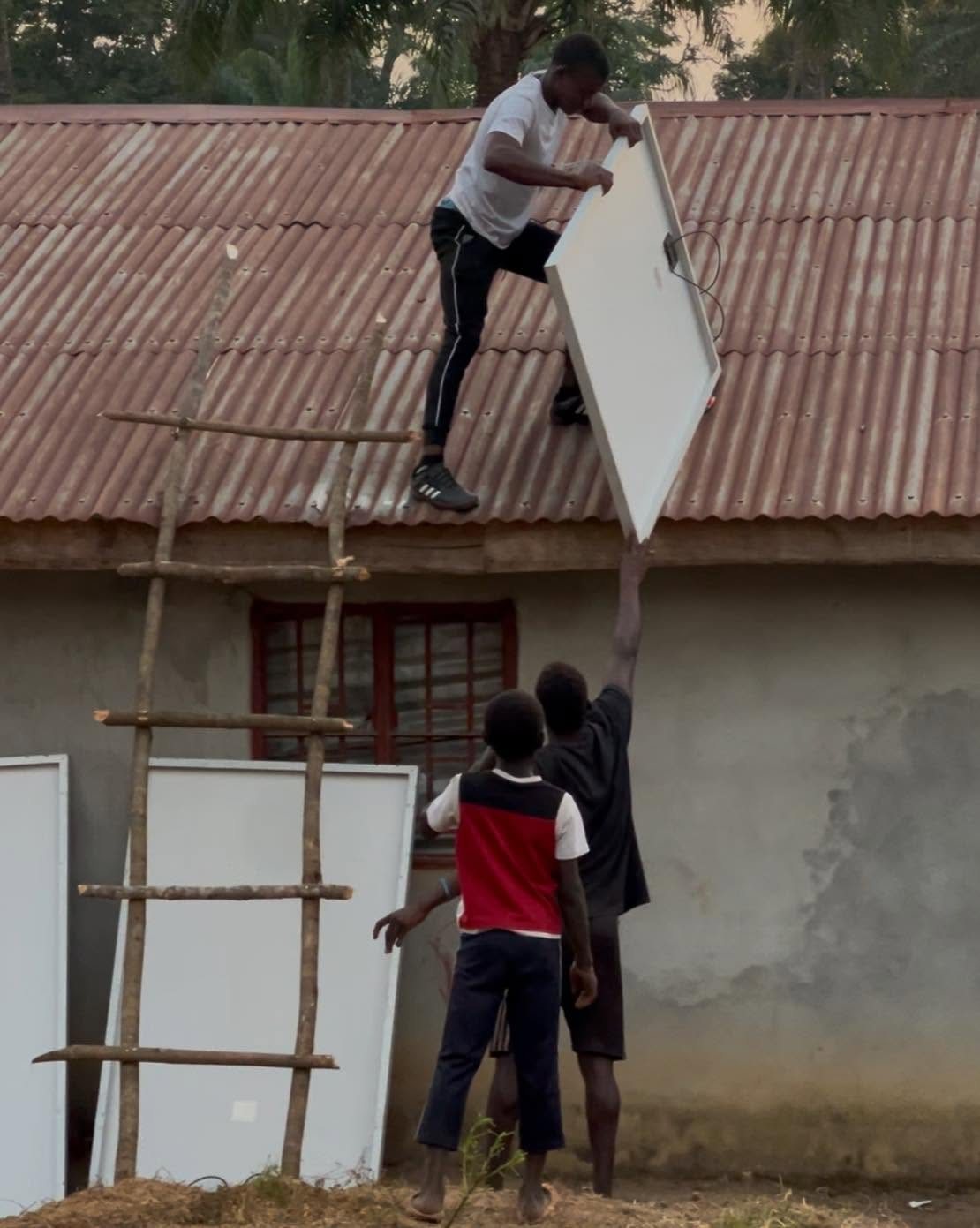 A young man lifting a solar panel onto a roof while others help from below